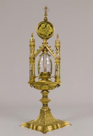 A gilded reliquary with a central clear crystal ovoid vessel.