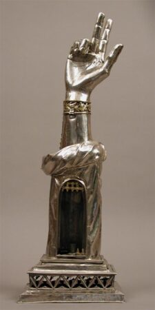 A silver reliquary in the shape of a forearm with three fingers raised.