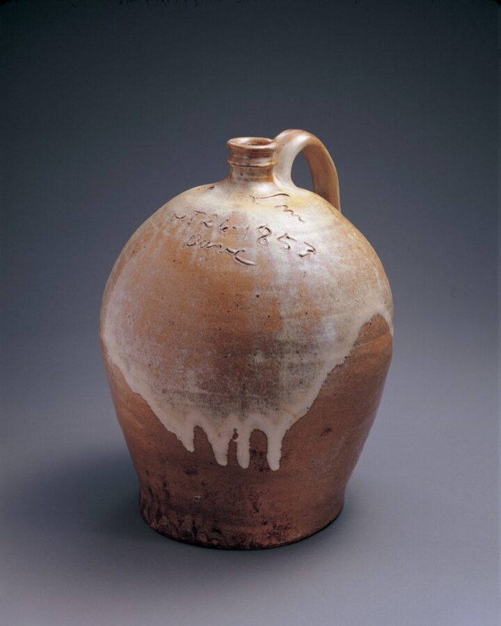 Photo of a fired clay-colored stoneware jug with a translucent coat of white glaze over its upper half.