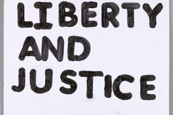 Black, painted text on a white poster board that reads ‘LIBERTY AND JUSTICE’.