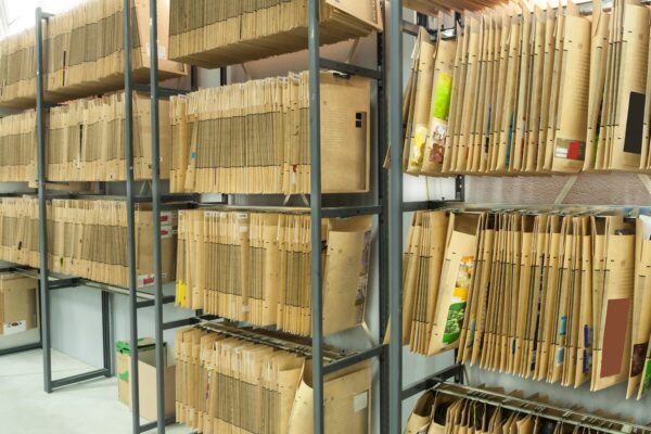 Rows of tall metal shelves filled with large brown archival folders organized in a storage room.