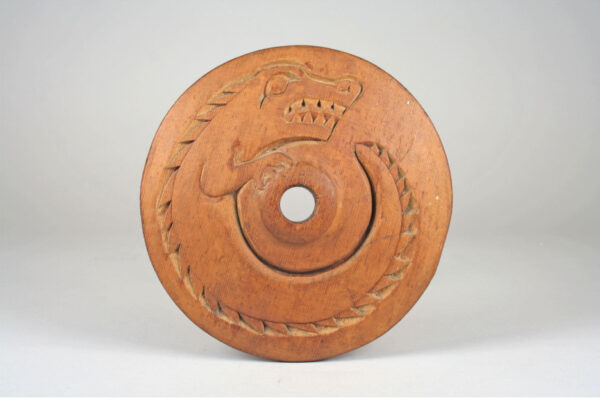 A wooden wheel is upright on display. The wheel includes engravings.