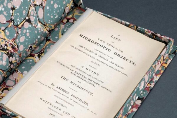 Open book titled A List of Two Thousand Microscopic Objects displayed in a marbled slipcase, showing its printed title page with detailed text by Andrew Pritchard.