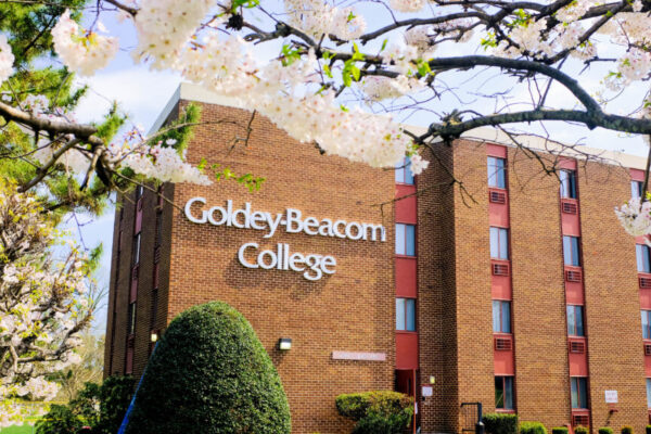 Exterior of a brick academic building with a “Goldey-Beacom College” sign, framed by blooming trees in spring.
