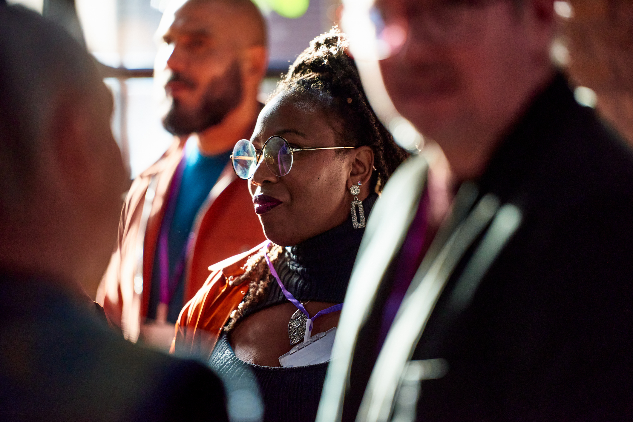 Attendees wearing conference badges engaged in conversation, with a woman in glasses in focus and others blurred in the foreground.