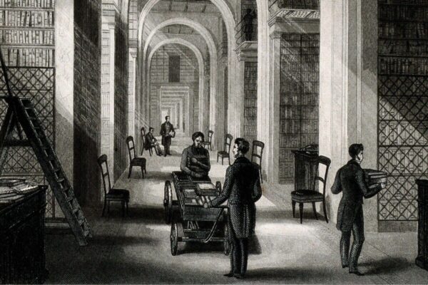 Black-and-white engraving of the British Museum’s Additional Library in 1844, showing a long vaulted hall lined with floor-to-ceiling bookshelves. Library staff and readers stand among book carts, ladders, chairs, and elevated gallery shelves beneath a series of repeating arches.
